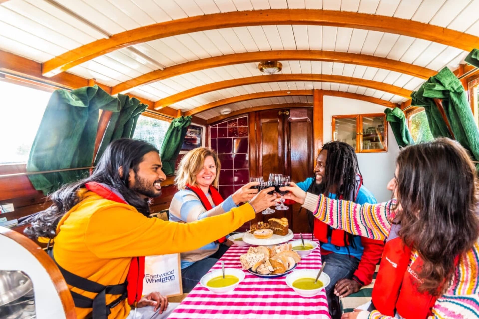 Four people enjoy some food and a drink inside a motorboat on the Norfolk Broads.