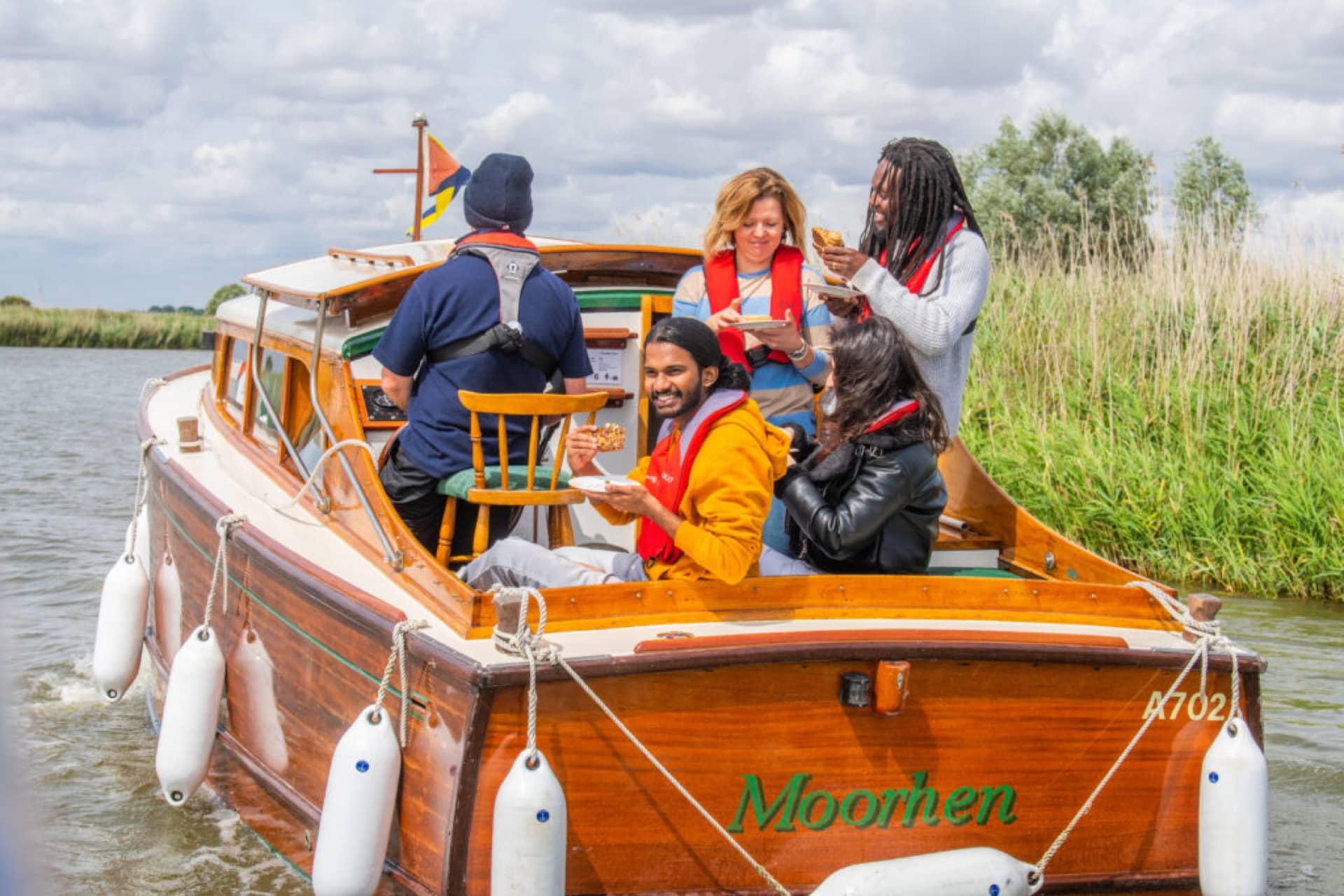 A group of people enjoy some food sitting and looking out of the back of a motorboat on the Norfolk Broads.