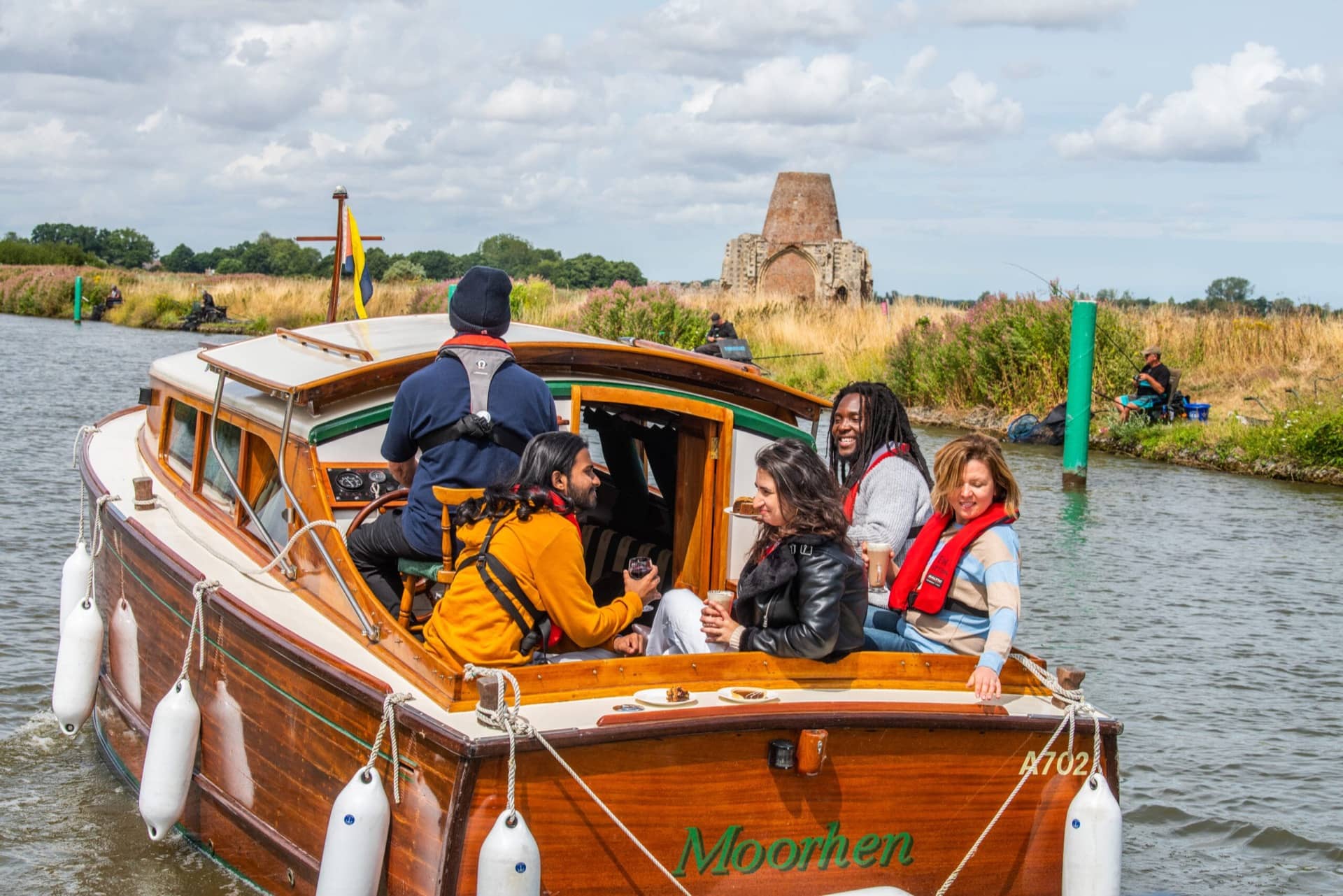A group of people enjoy a drink sitting and looking out of the back of a motorboat on the Norfolk Broads.