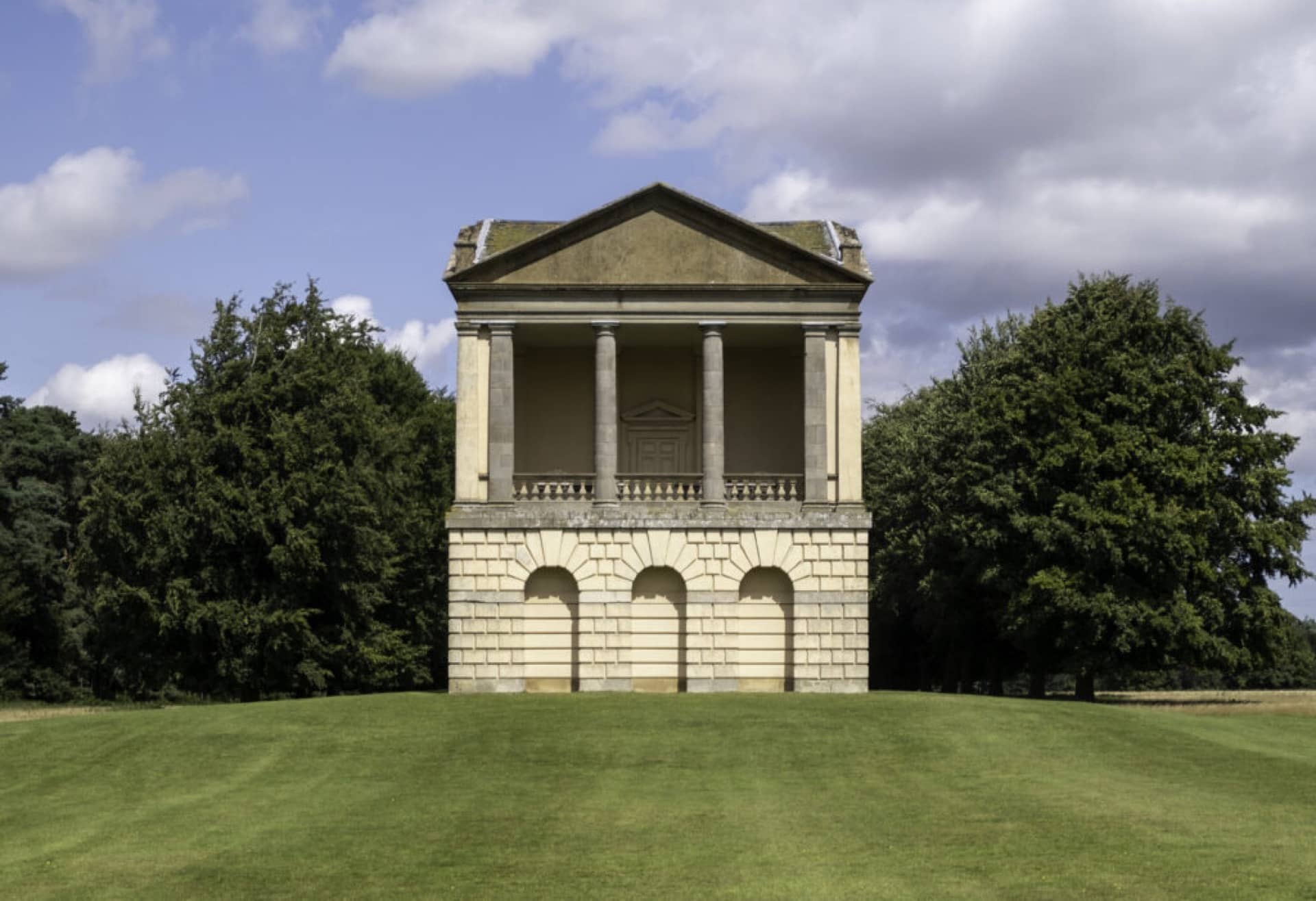 The water tower folly in light brick in the grounds of Houghton Hall, Kings Lynn surrounded by grass and trees on a sunny day