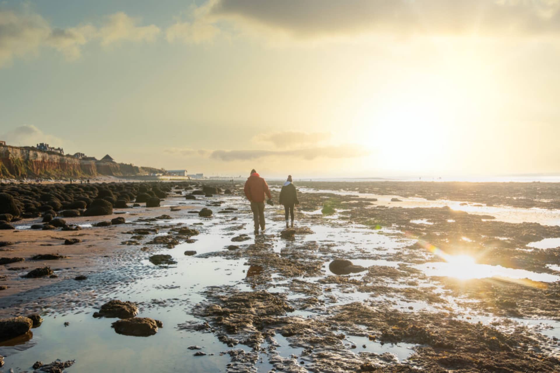 A couple walking on the beach at sunset with rocks and the Hunstanton cliffs in the background