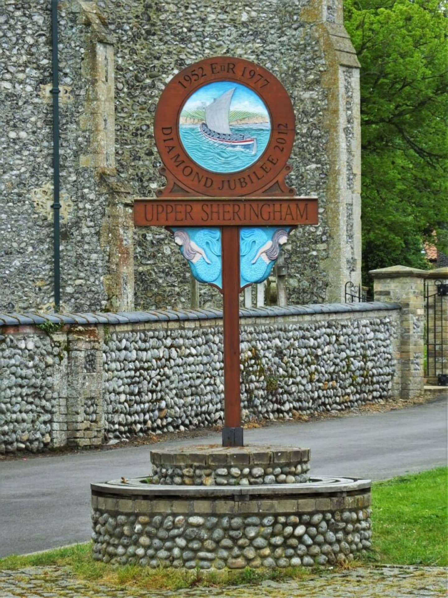 The sign for Upper Sheringham next to a stone church.