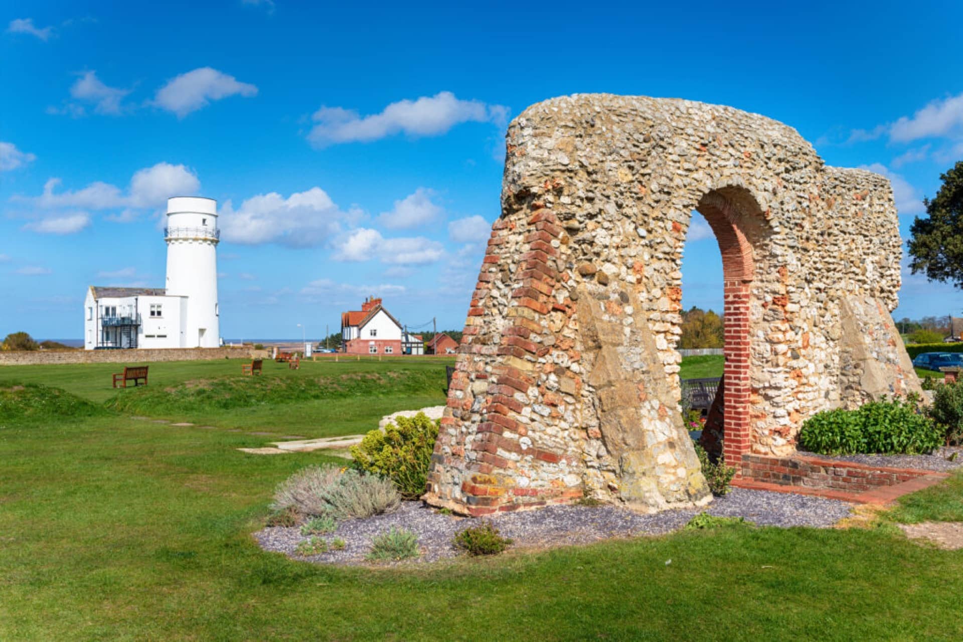 The ruins of St Edmund's chapel in the foreground surrounded by grass with benches and the Hunstanton lighthouse in the background on a sunny day in Hunstanton, Norfolk