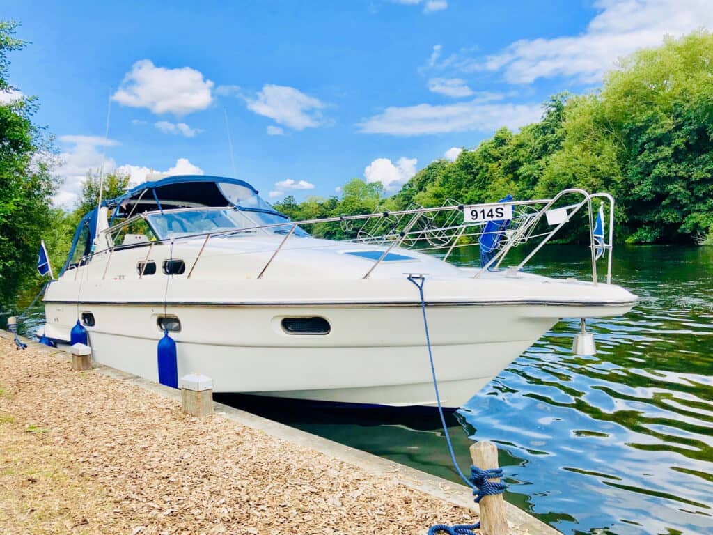 A boat moored up along the Norfolk Broads next to a path with trees lining the other side of the river on a sunny day in Norfolk