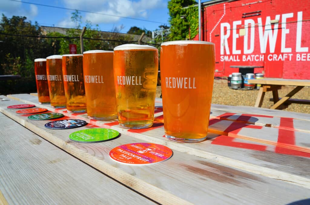 Six pints of Redwell beer on a picnic table in the sun