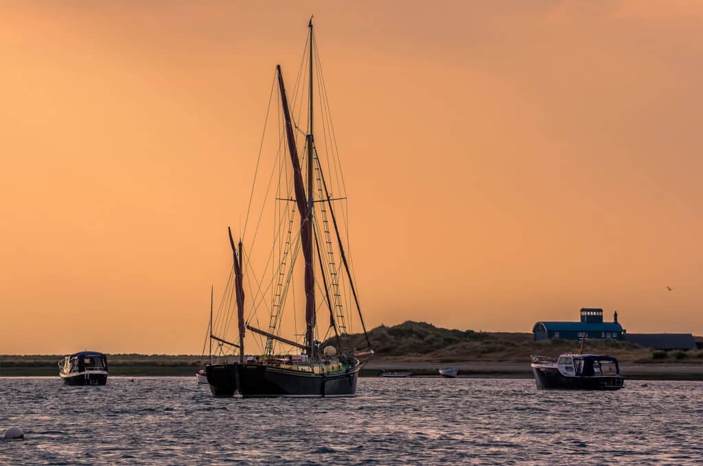 Boats moored at Blakeney Point on the water in Norfolk looking towards the lifeboat station in the distance just before sunset