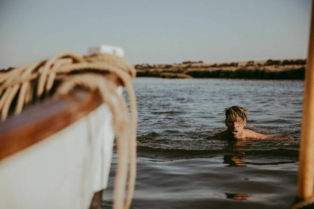 A man swimming towards an out-of-focus boat in the foreground