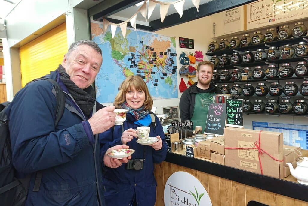 Two people drinking a cup of tea with stallholder in background alongside different loose tea