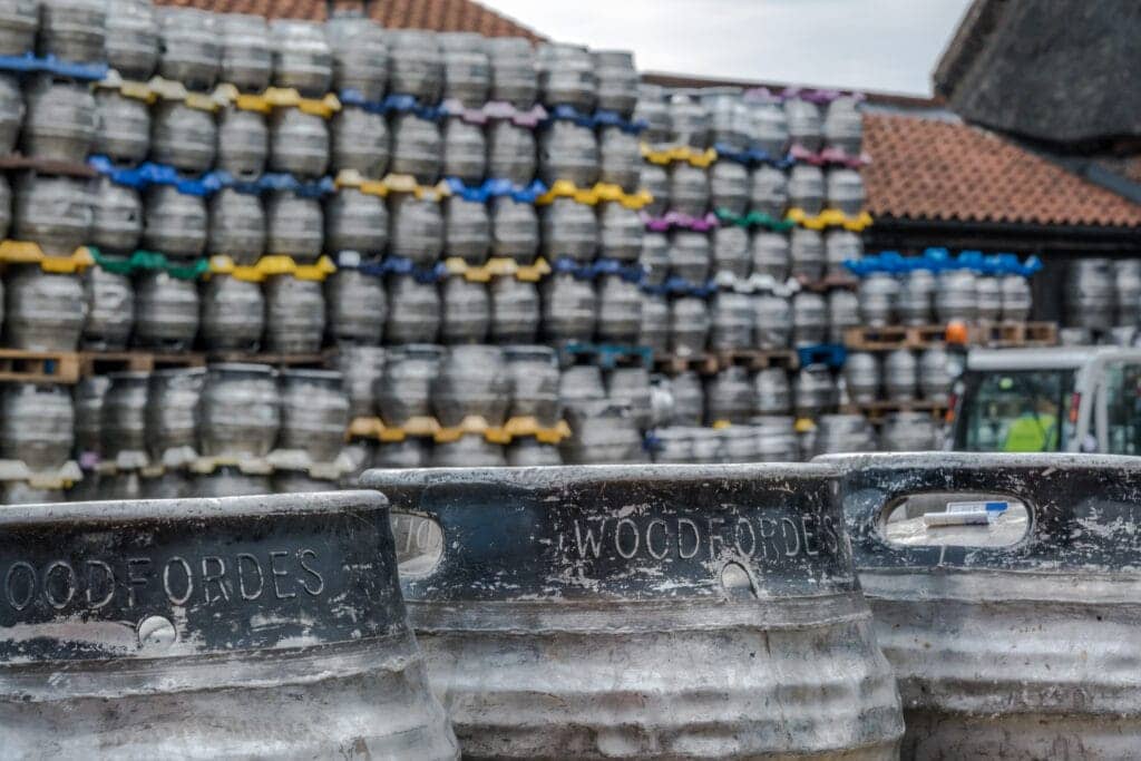 Three kegs in the foreground that read "Woodforde's" and stacked kegs on pallets behind