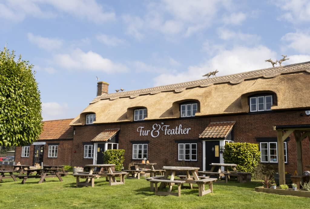 Picnic tables on grass outside the front of Fur and Feather in the sun