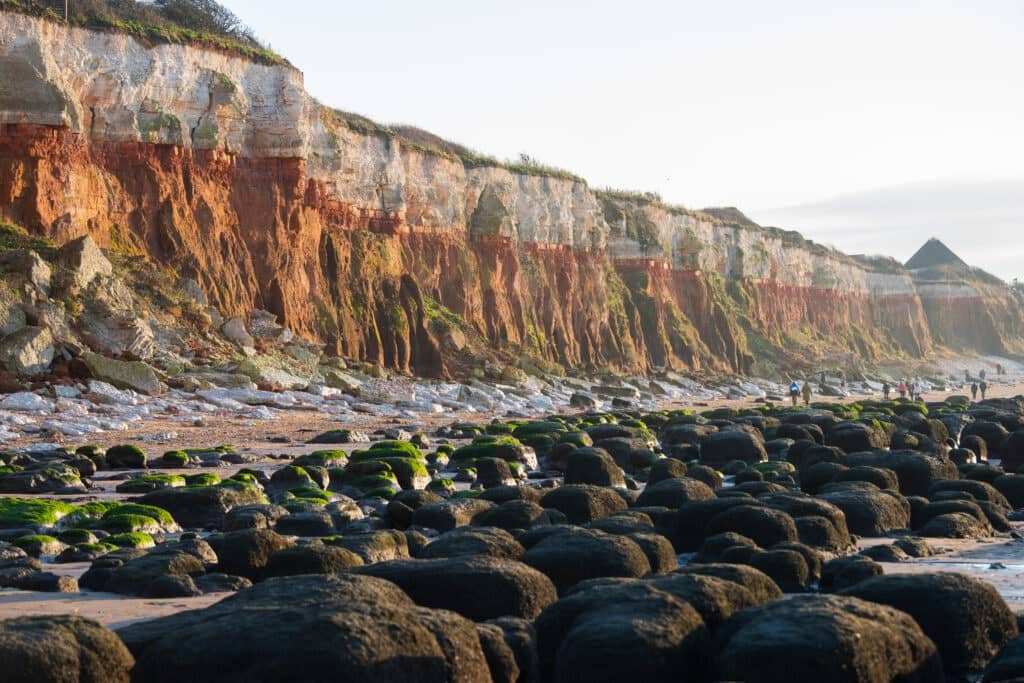 A group of people walk down a rocky beach next to the Hunstanton Cliffs.