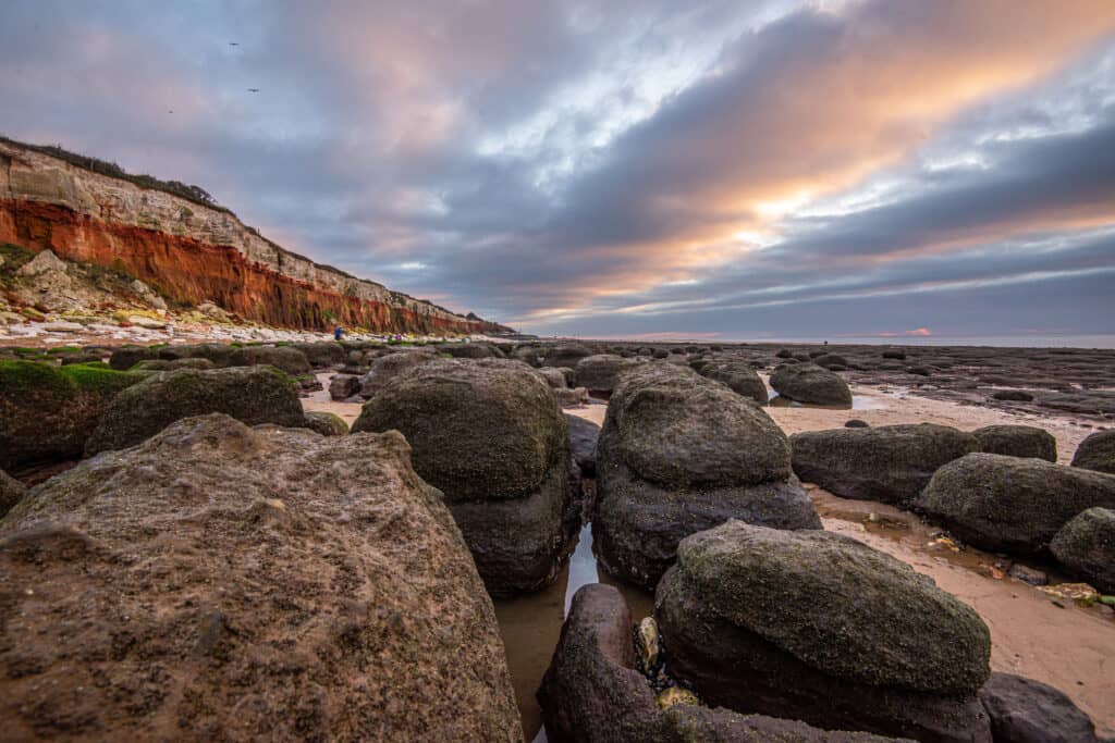 Large rocks are line Hunstanton beach with the cliffs in the background on a cloudy day.