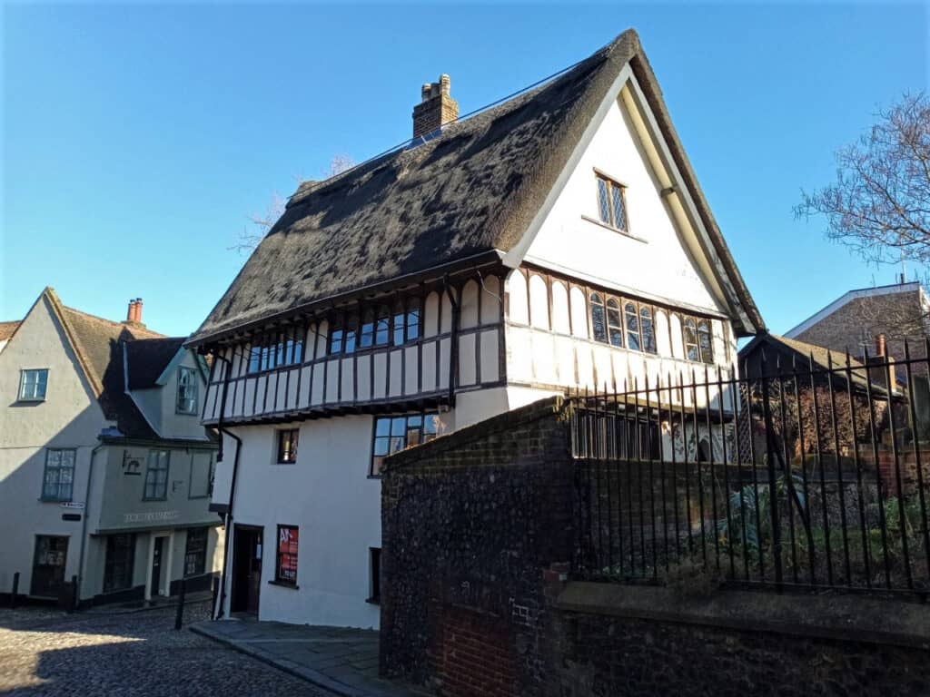 A white building with a thatched roof on a cobbled street.