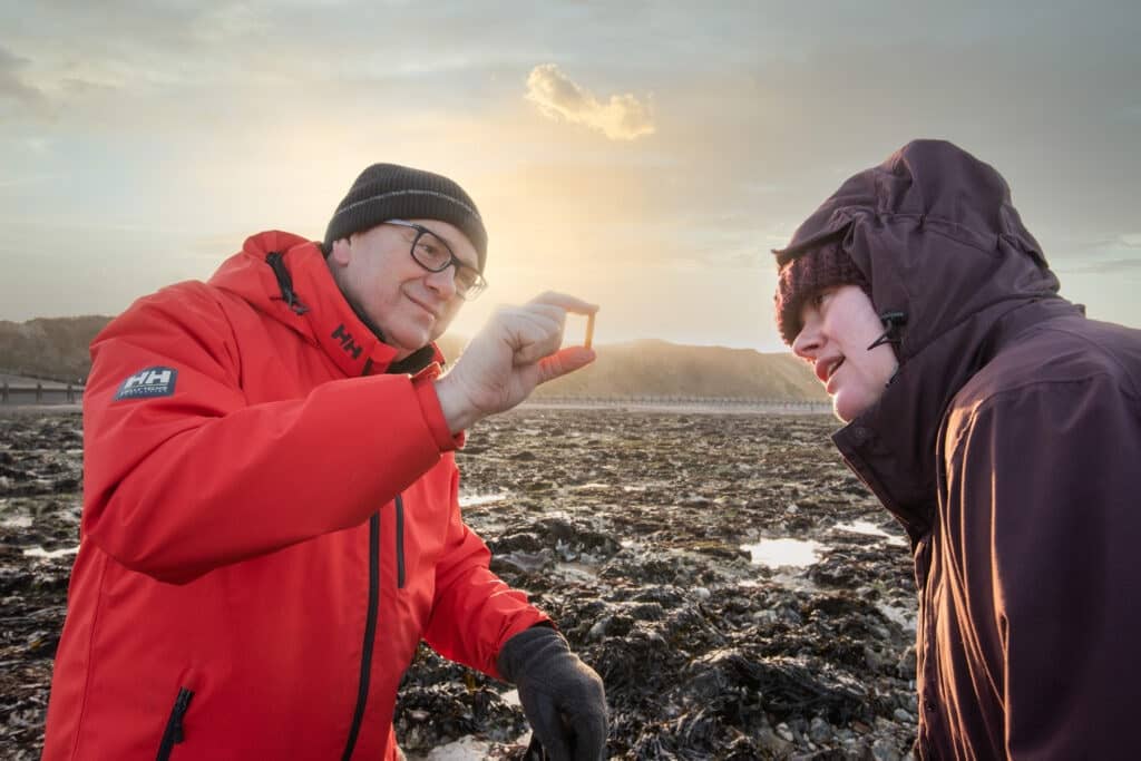 Two people look at a rock on West Runton Beach.