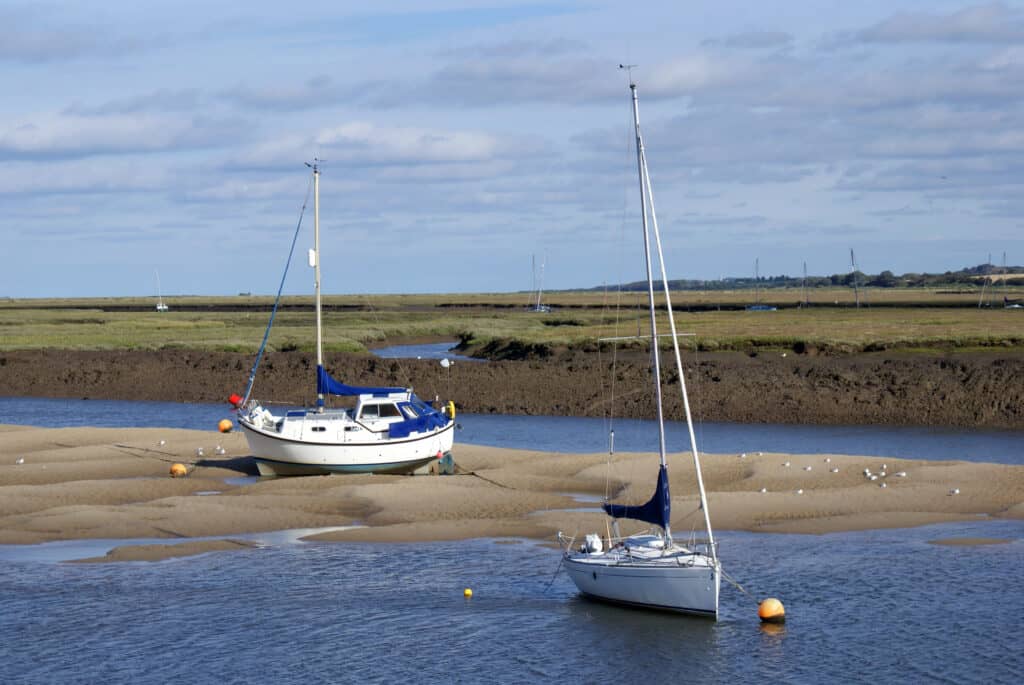 One boat anchored in the river and another on a sandbank at Blakeney harbour at low tide