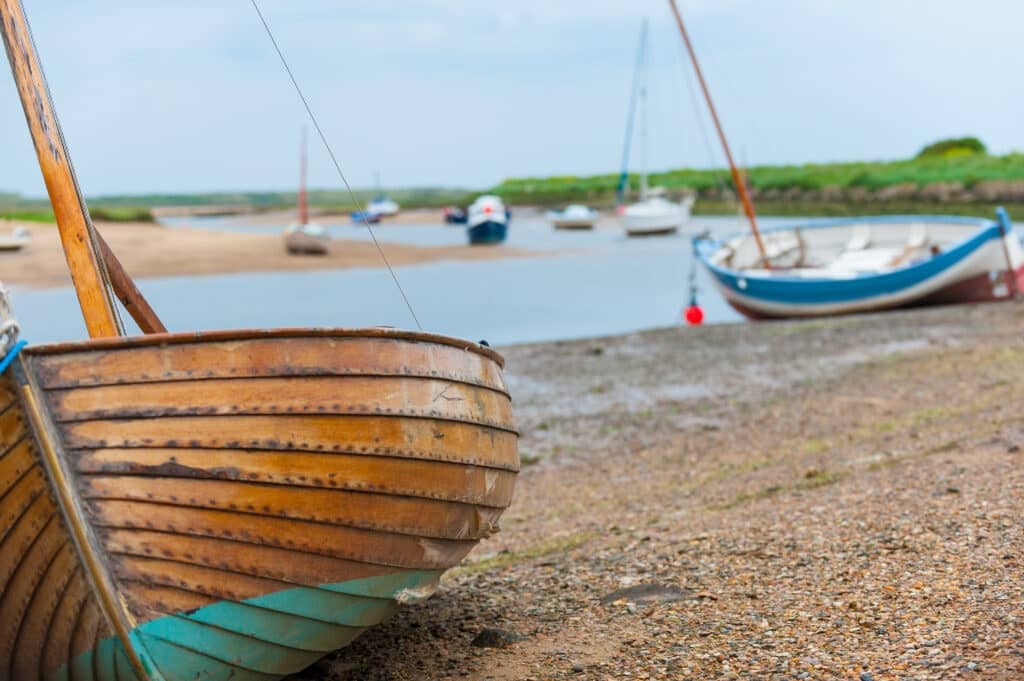Boats moored up on the beach at Brancaster Staithe with other boats on the water in the background on a sunny day