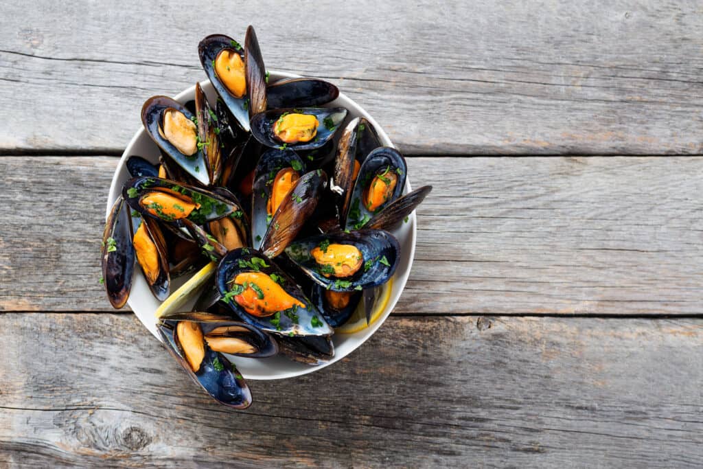 Cooked mussels presented in a white bowl on a wooden table