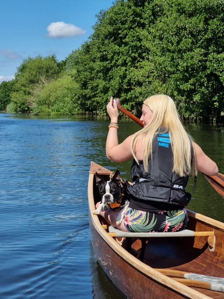 Woman at front of canoe with a dog accompanying