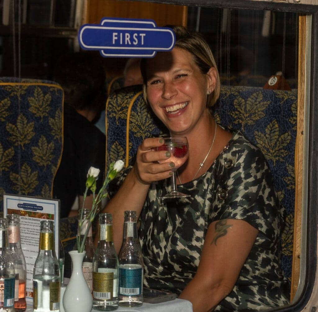 A woman riding the steam train looking out the window with a glass of gin.