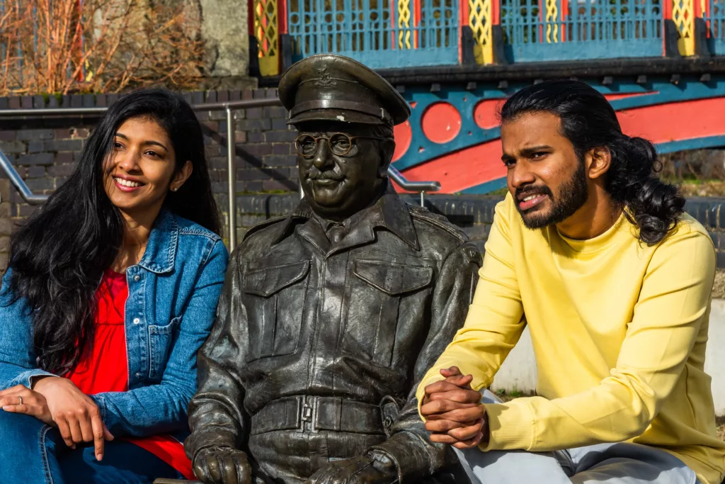 Two people sitting next to a statue of Captain Mainwaring from "Dad's Army"