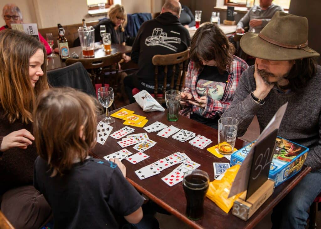 Four people sitting at a table with drinks and playing a card game