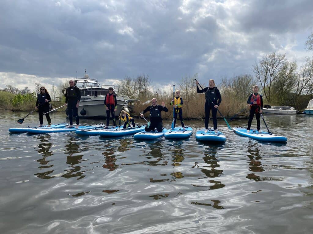 A group of people paddleboarding down the Norfolk Broads.