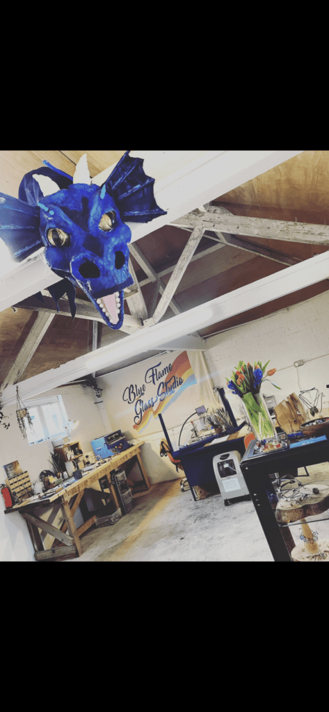 Inside a workshop studio with art supplies and a blue dragon head posed at the top of the ceiling.