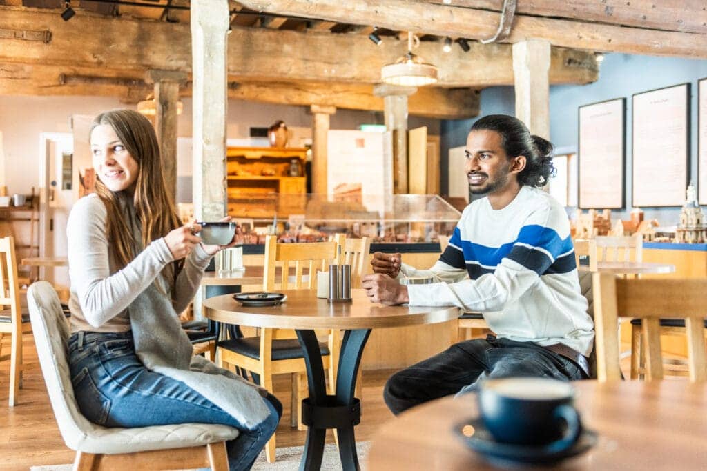 A man and a woman enjoy a hot drink in a cafe at a wooden table.