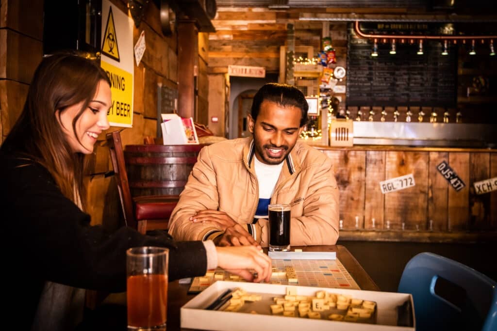 A man and a woman play scrabble at a table inside Nip and Growlers Ale House in Norfolk.