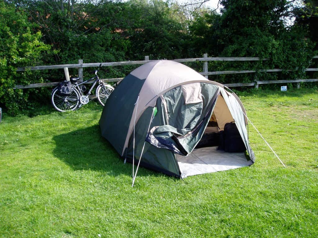 A tent pitched in a field with a bike behind it resting against a fence.