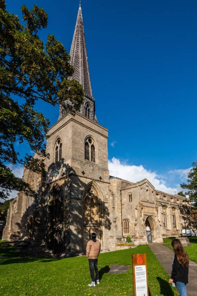 A man and a woman stand outside a Norfolk Church on a sunny day.