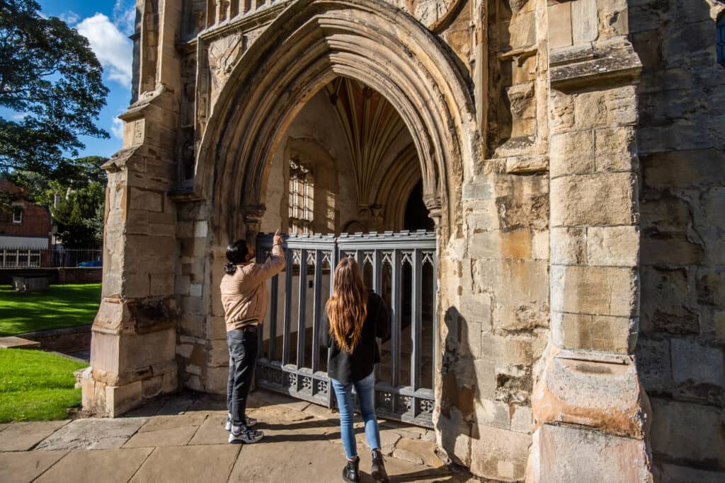 A man and a woman stand outside a Norfolk Church on a sunny day.