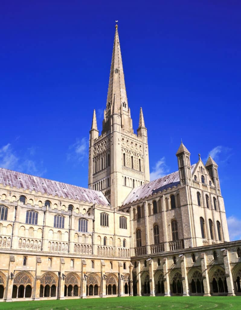 The outside of Norwich Cathedral capturing the tall spire on a sunny day.