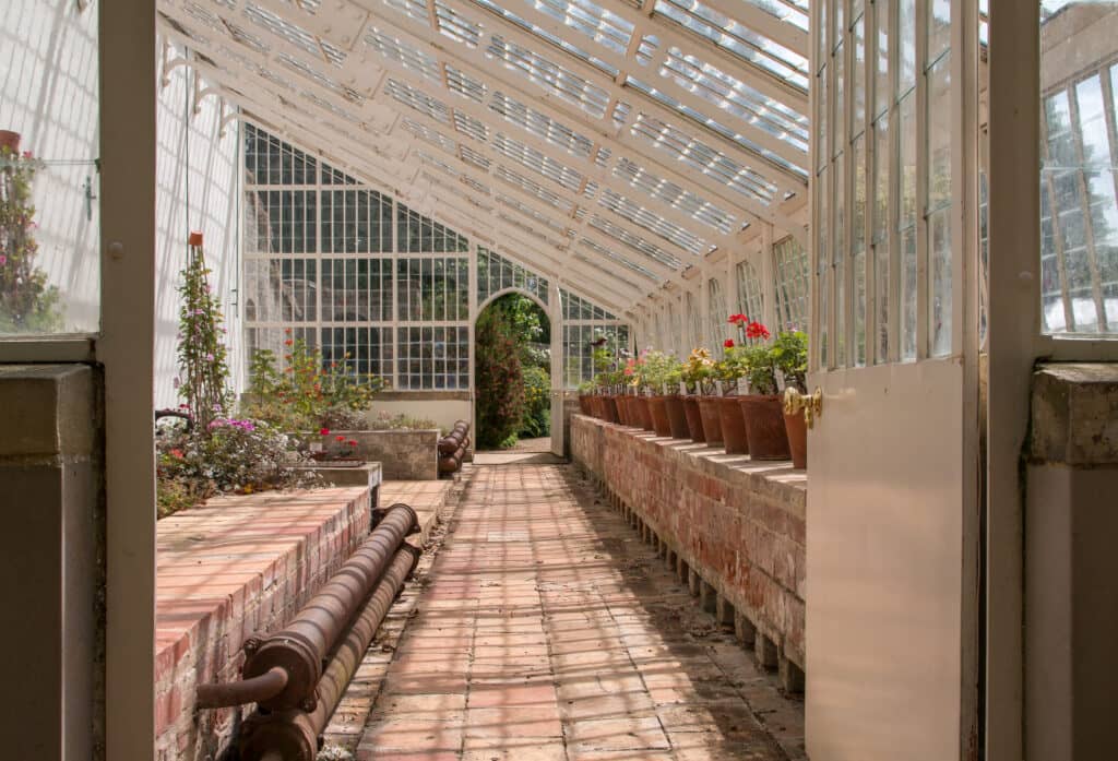 The inside of a glass house attached to a stately home with a path and some plants inside in Norfolk.