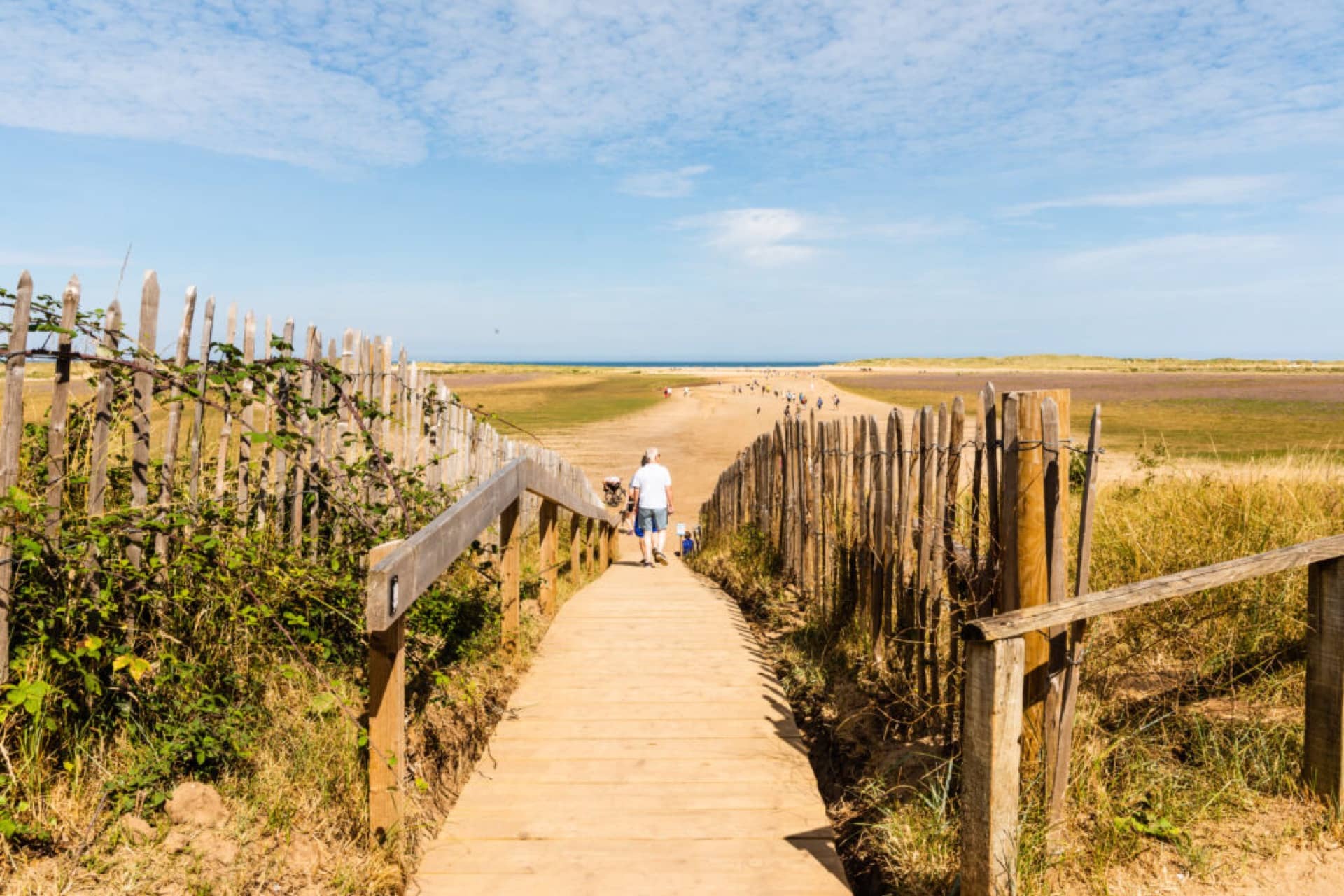 People walking down a wooden path to Holkham beach on a sunny day