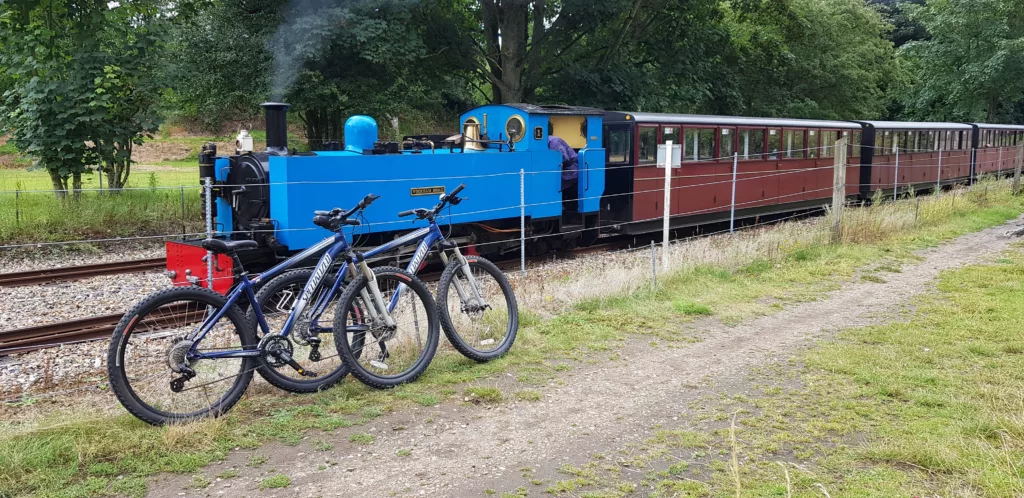 Two bikes parked up as a steam train goes past on the Bure Valley Railway