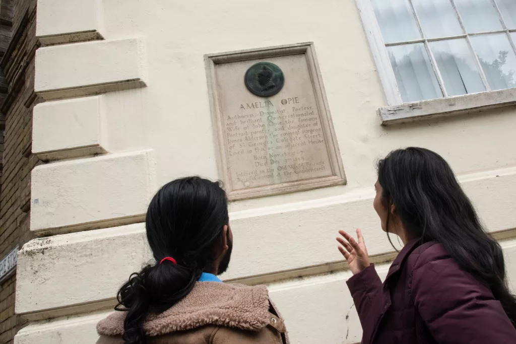 Two people reading a plaque to Amelia Opie