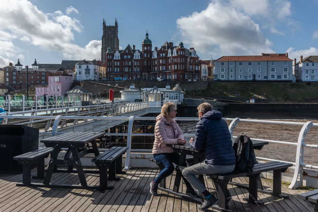 Two people sitting on a bench at Cromer Pier facing Cromer town centre