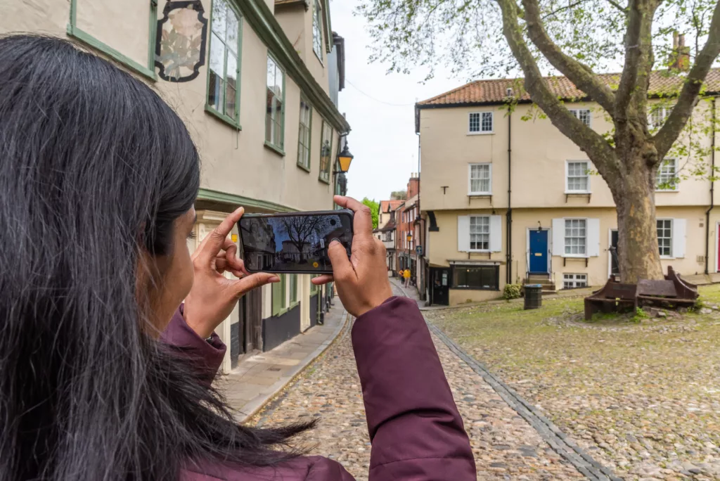 A woman taking a photo of a London Plane in Elm Hill, Norwich