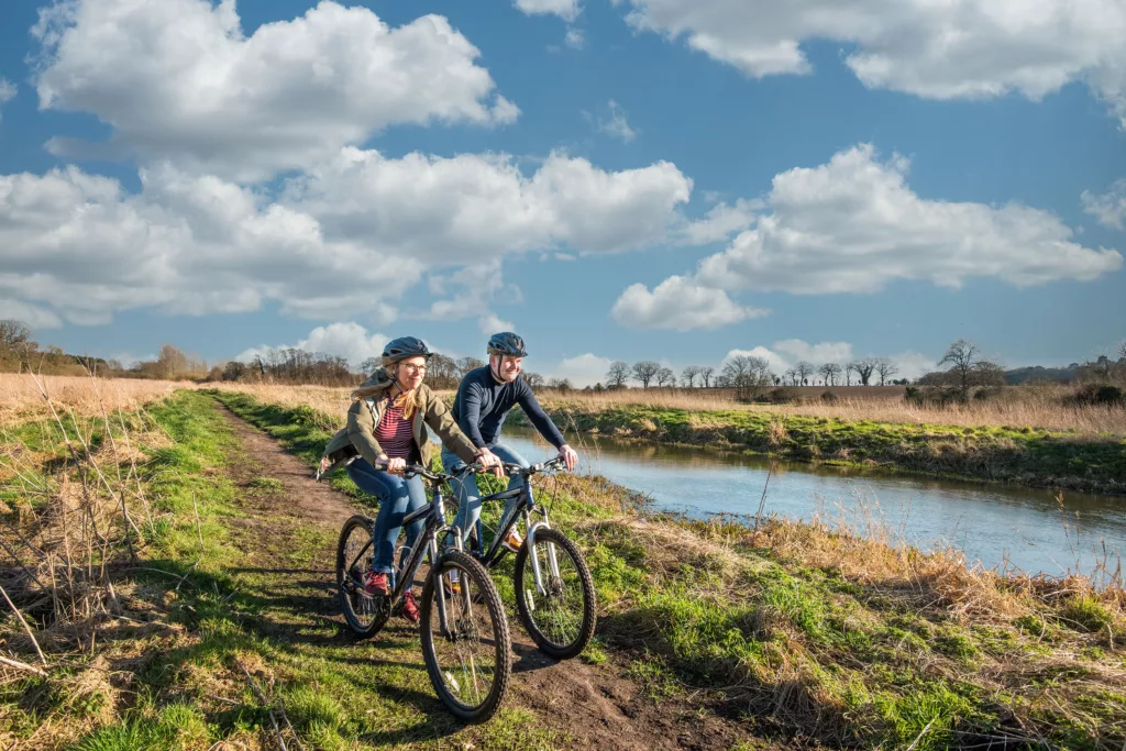 Two people riding bikes next to a river