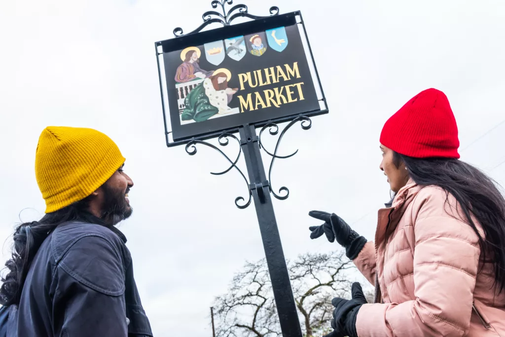 Two people stood underneath the Pulham Market town sign