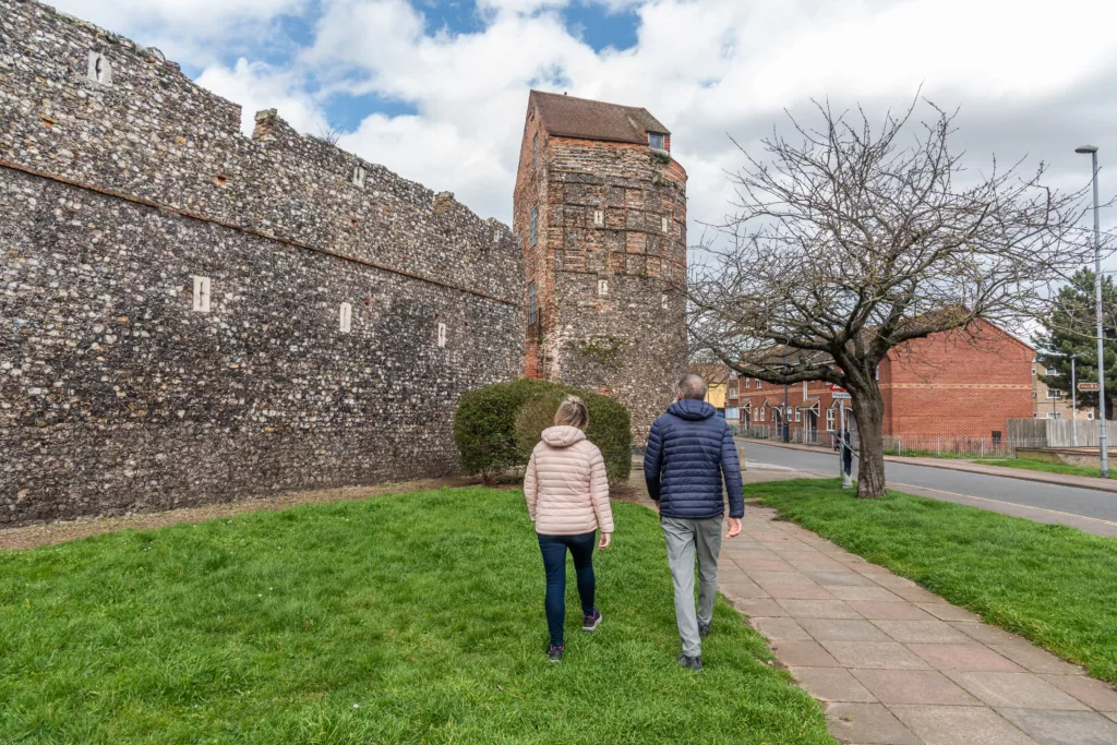 Two people walking past a medieval flint town wall in Great Yarmouth