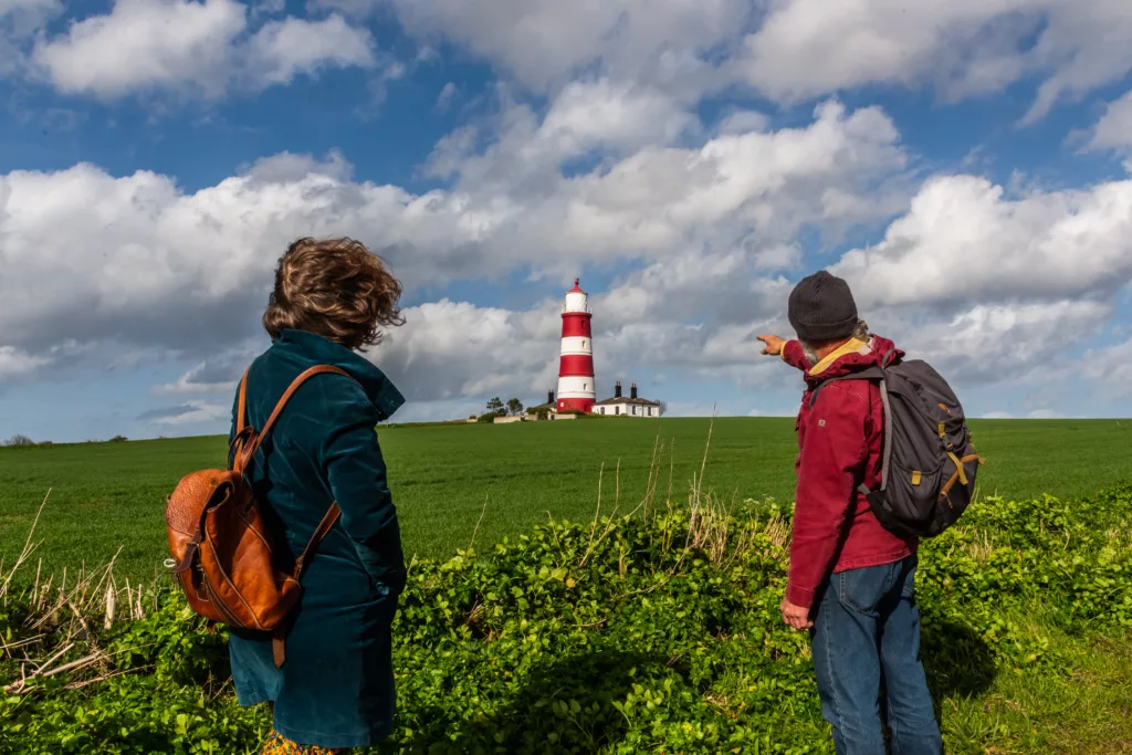 A woman standing next to a man pointing at Happisburgh Lighthouse in the distance