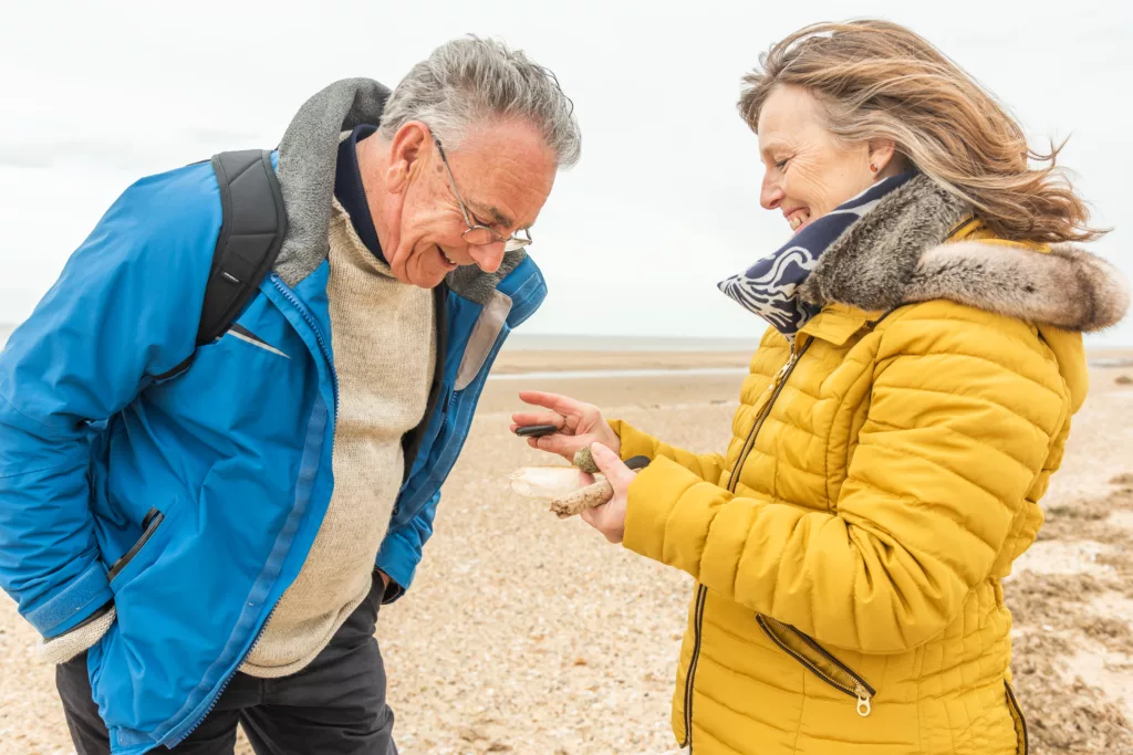 A smiling woman holding and showing objects found on the beach to a man