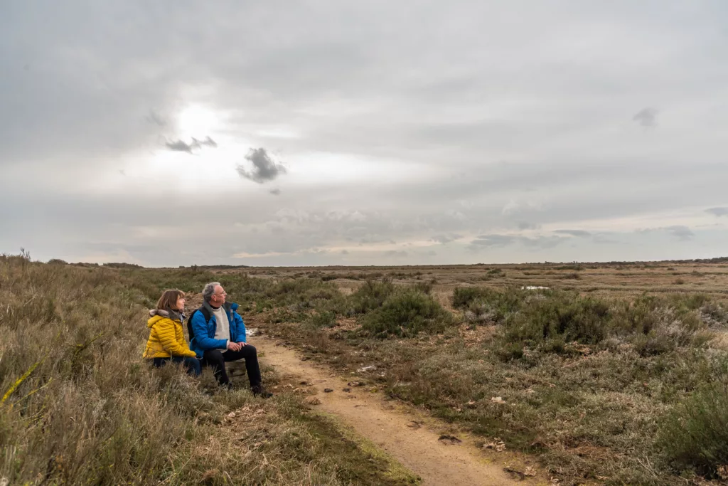 Two people sitting down next to a gravel path looking towards the distance