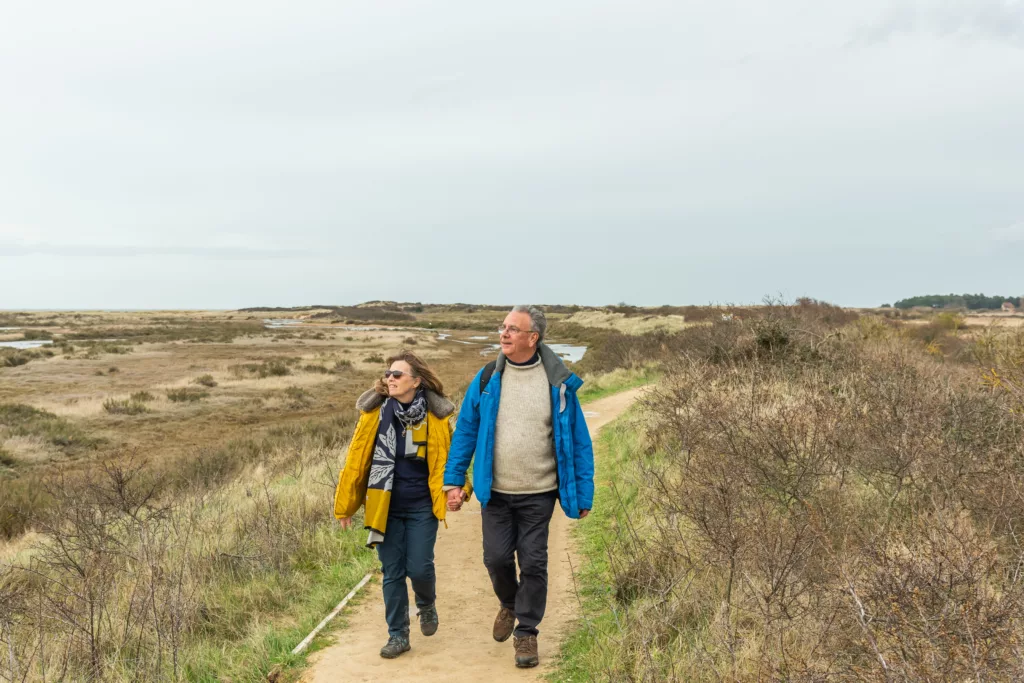 A man and a woman walking along a sandy path on an overcast day