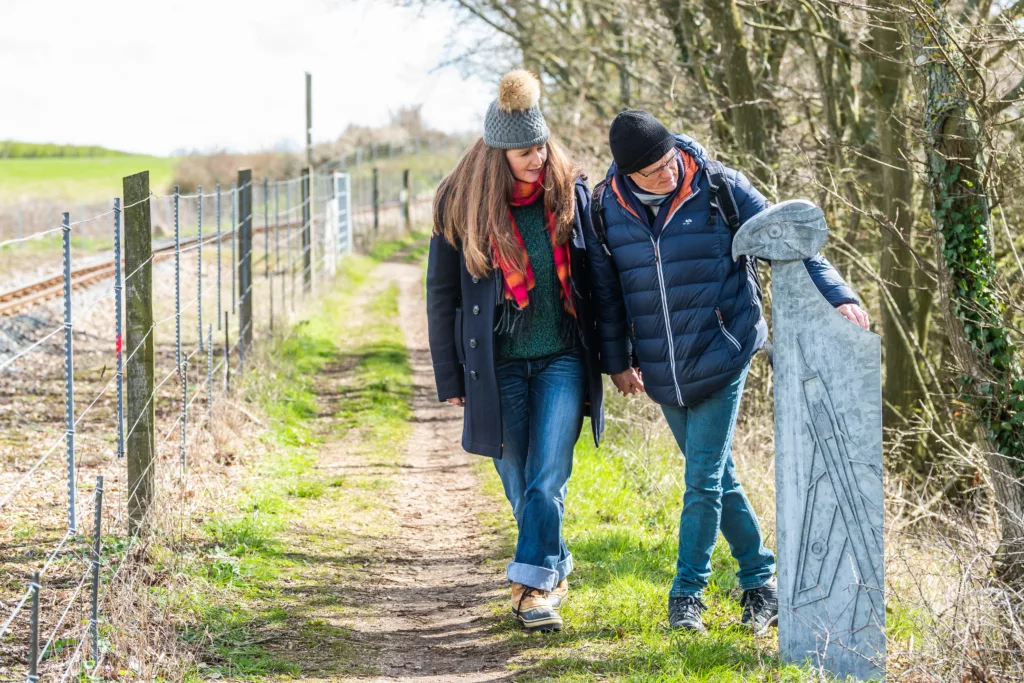 Two people looking at a carved goshawk head on a waymarker post