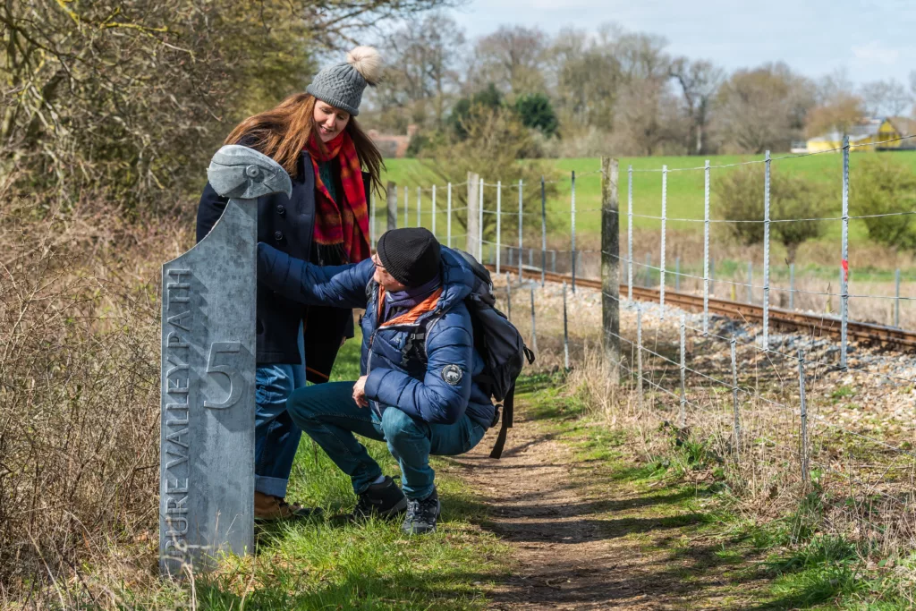 Two people looking at a carved goshawk head on a waymarker post with text reading "Bure Valley Path 5"