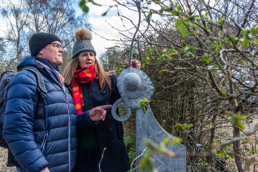 Two people looking at a carved butterfly head on a waymarker post