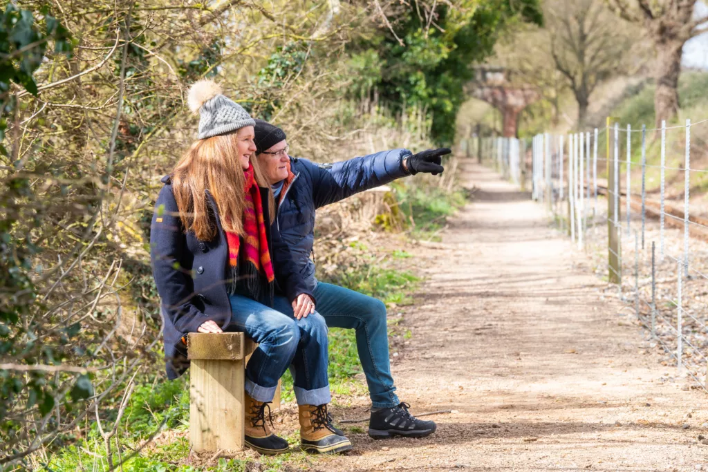 A man and woman sitting on a bench next to a gravel path